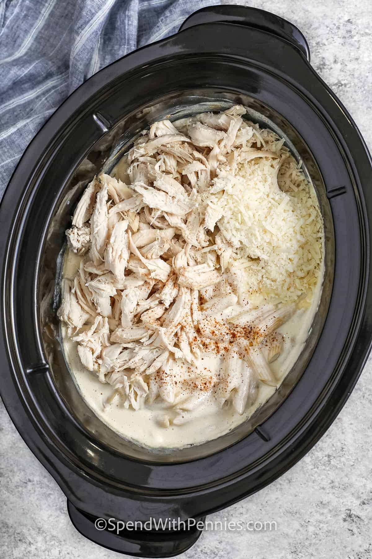 adding cooked chicken and cheese to pot to make Crock Pot Chicken Alfredo