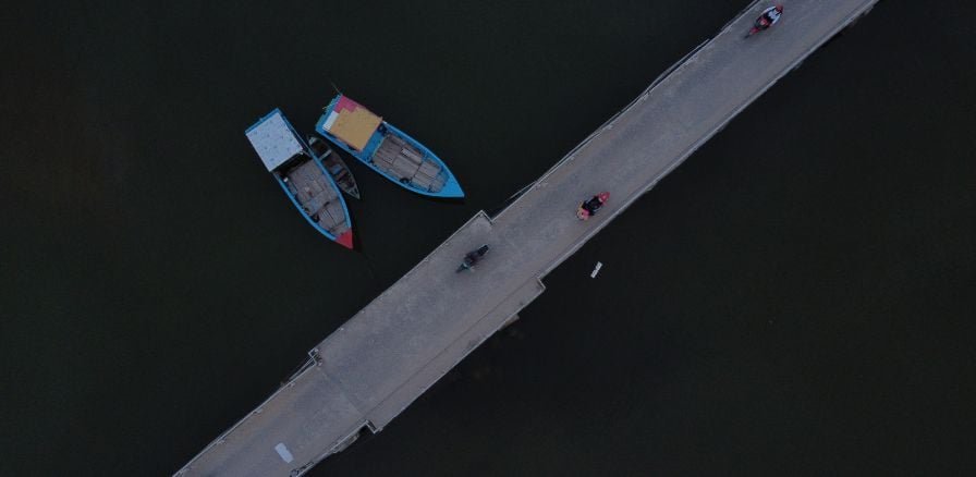 example of bridge in Vietnam, two boats to side of bridge and scooters crossing over 