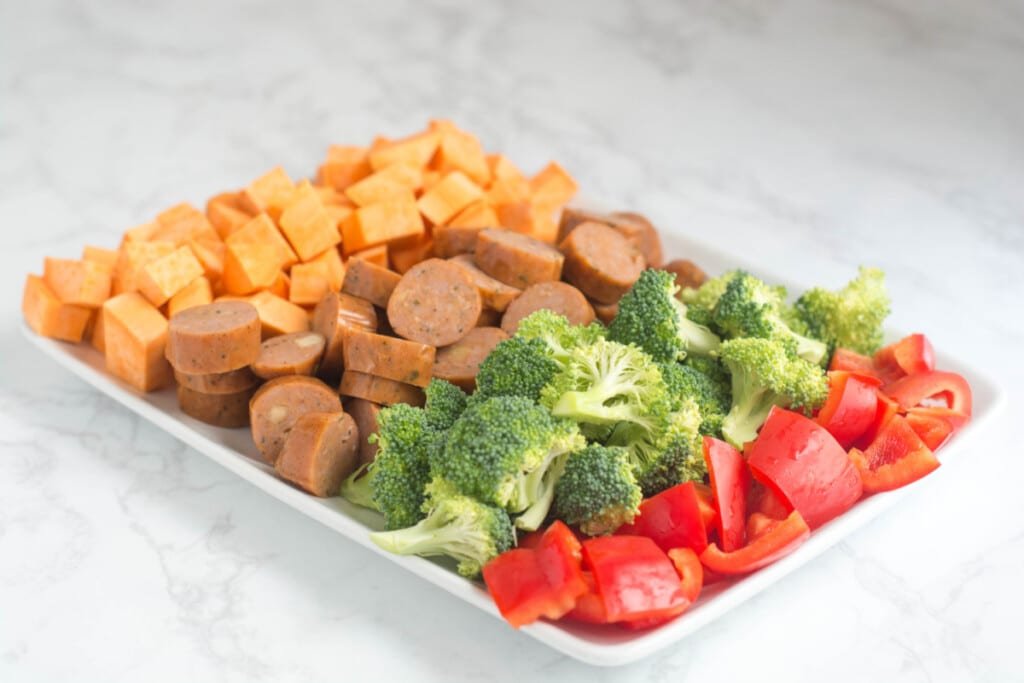 A white plate with cut-up sweet potatoes, sausage, broccoli, and red pepper.