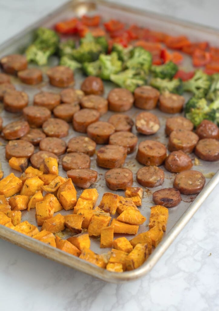 A baked pan of Sheet Pan Chicken Sausage & Veggies sits on a white countertop.