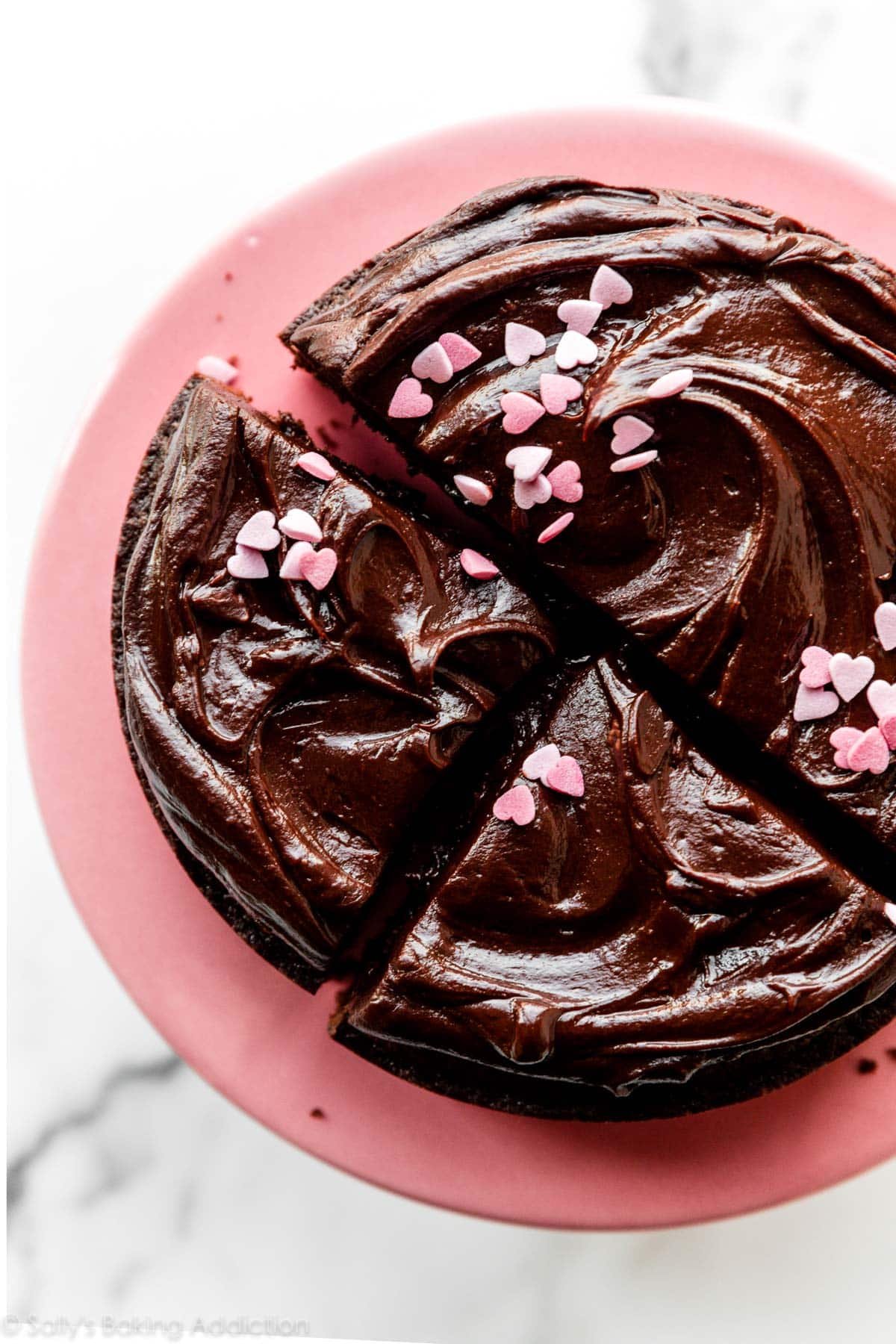 overhead photo of chocolate ganache and pink heart sprinkles on a chocolate cake