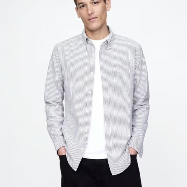 a man wearing a long sleeve button front oxford style shirt over a crewneck shirt and pants